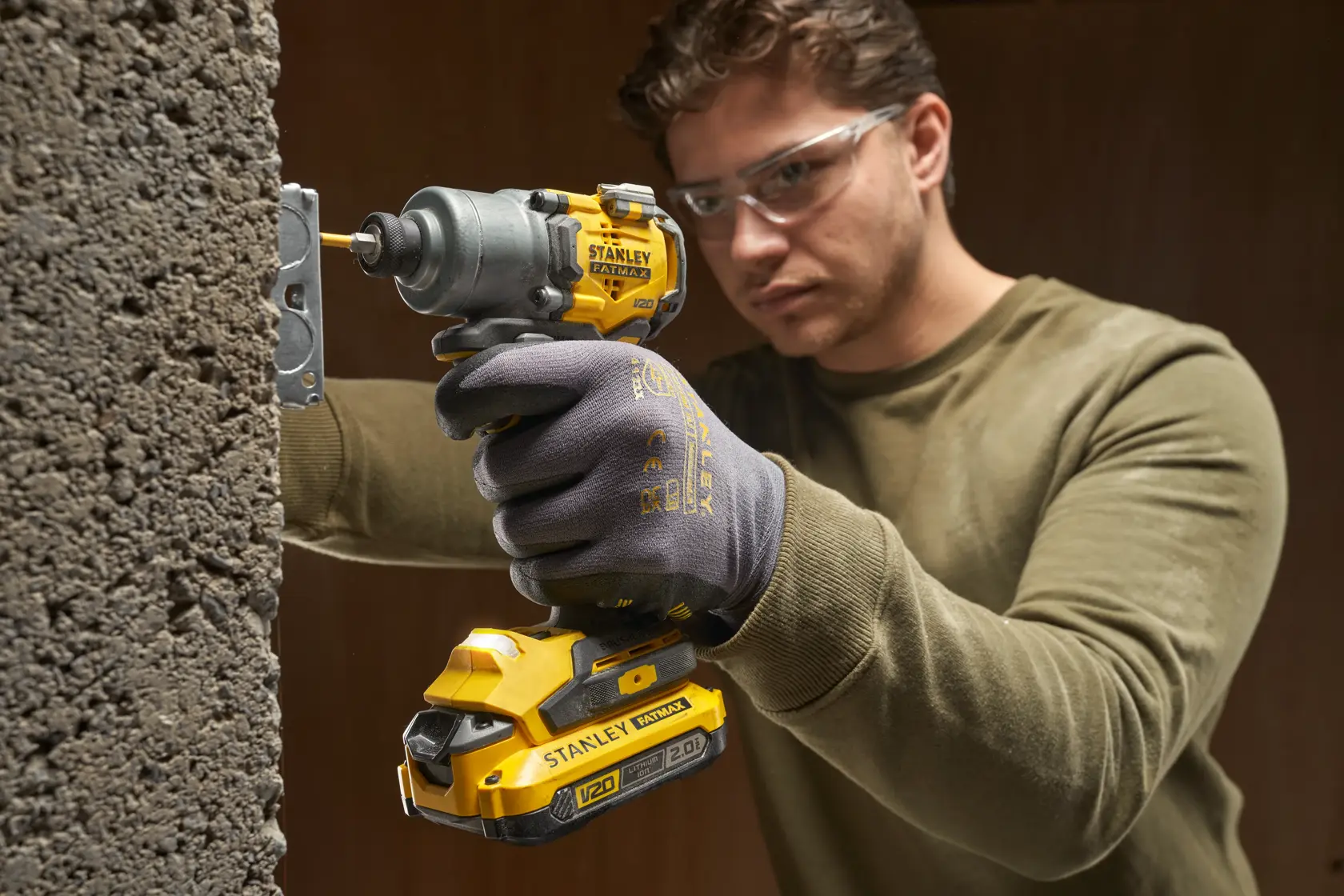Photo of worker using STANLEY SFMCF830D2K cordless impact driver with yellow and black design on concrete wall.