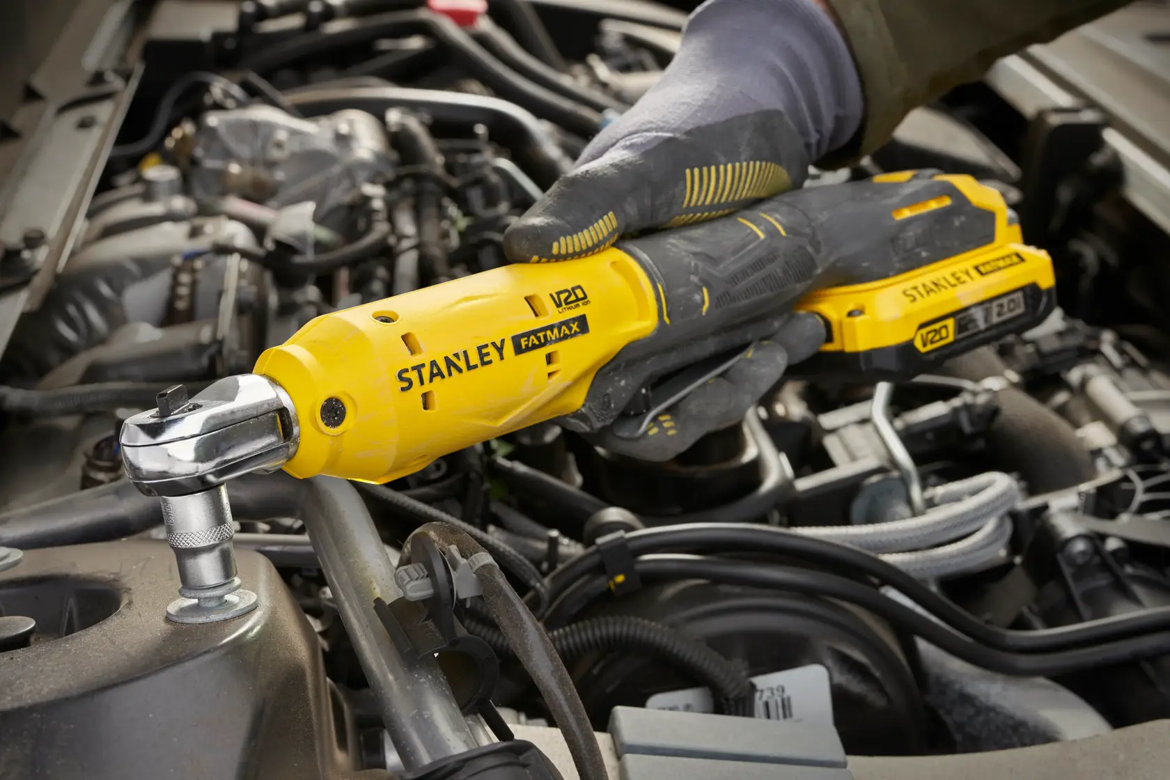 Photo of STANLEY SFMCF930B cordless ratchet tool in use tightening a bolt in a car engine compartment.