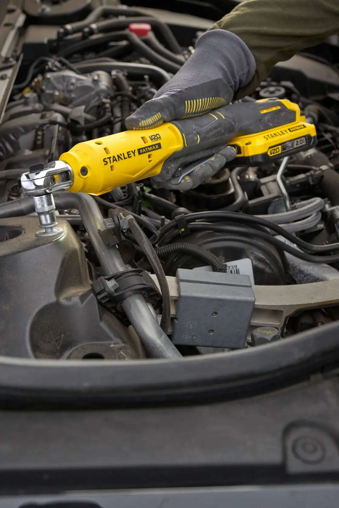 Photo of STANLEY SFMCF930B cordless ratchet tool being used on car engine by gloved hand.