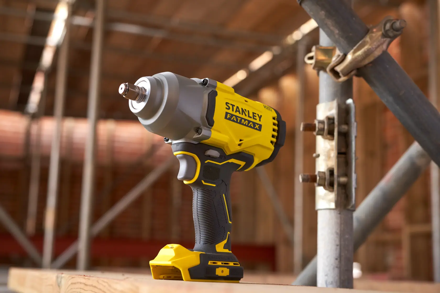 STANLEY SFMCF940B cordless impact wrench, yellow and black, shown upright on wooden surface at construction site.