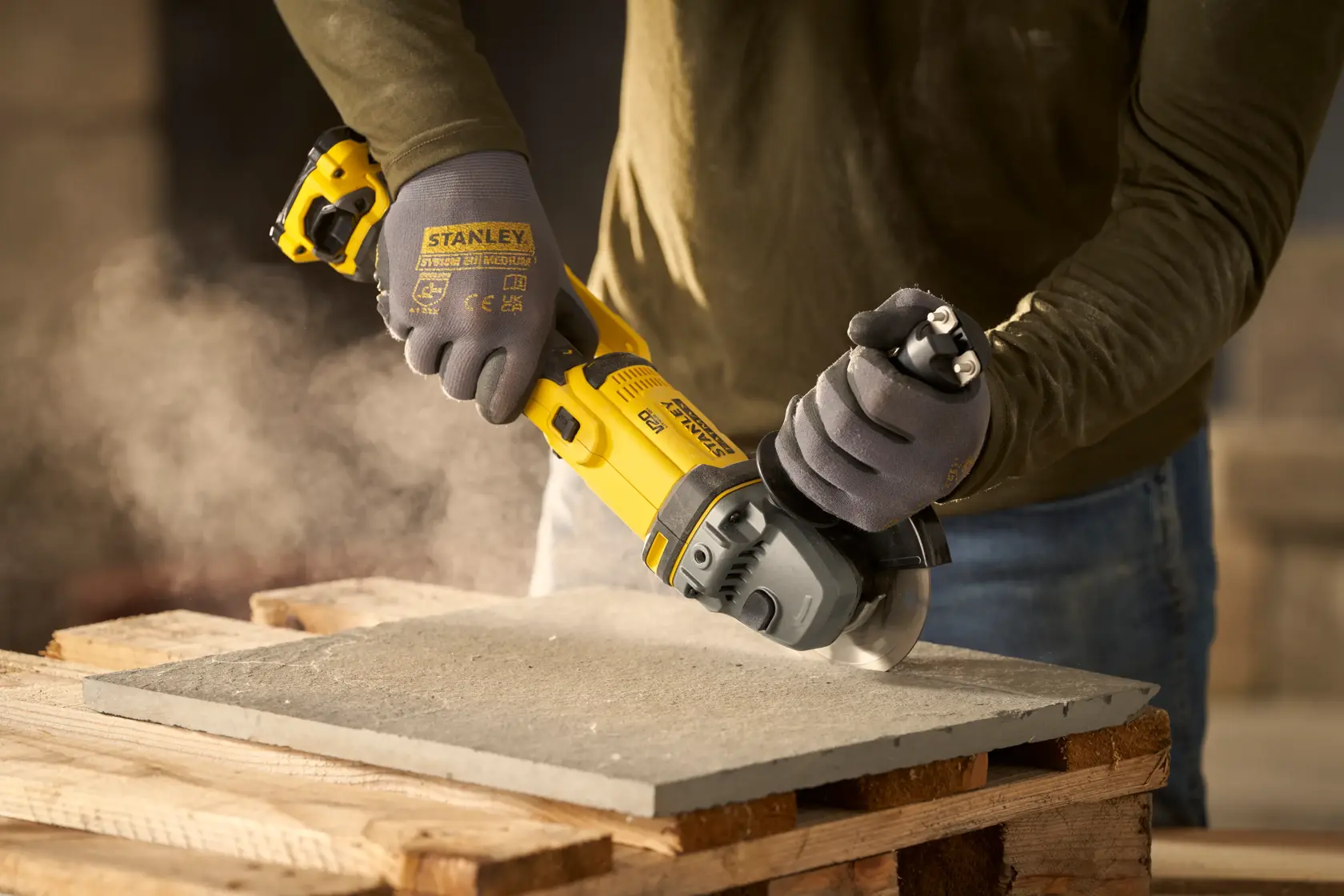 STANLEY SFMCG300B angle grinder in use cutting a concrete slab, close-up of hands wearing gloves.