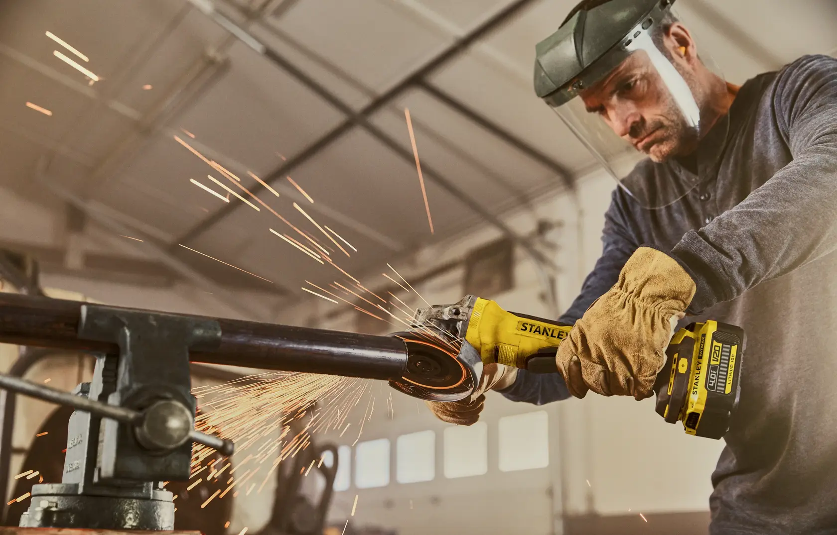 Photo of STANLEY SFMCG700B cordless angle grinder in use, cutting metal pipe with sparks in workshop.