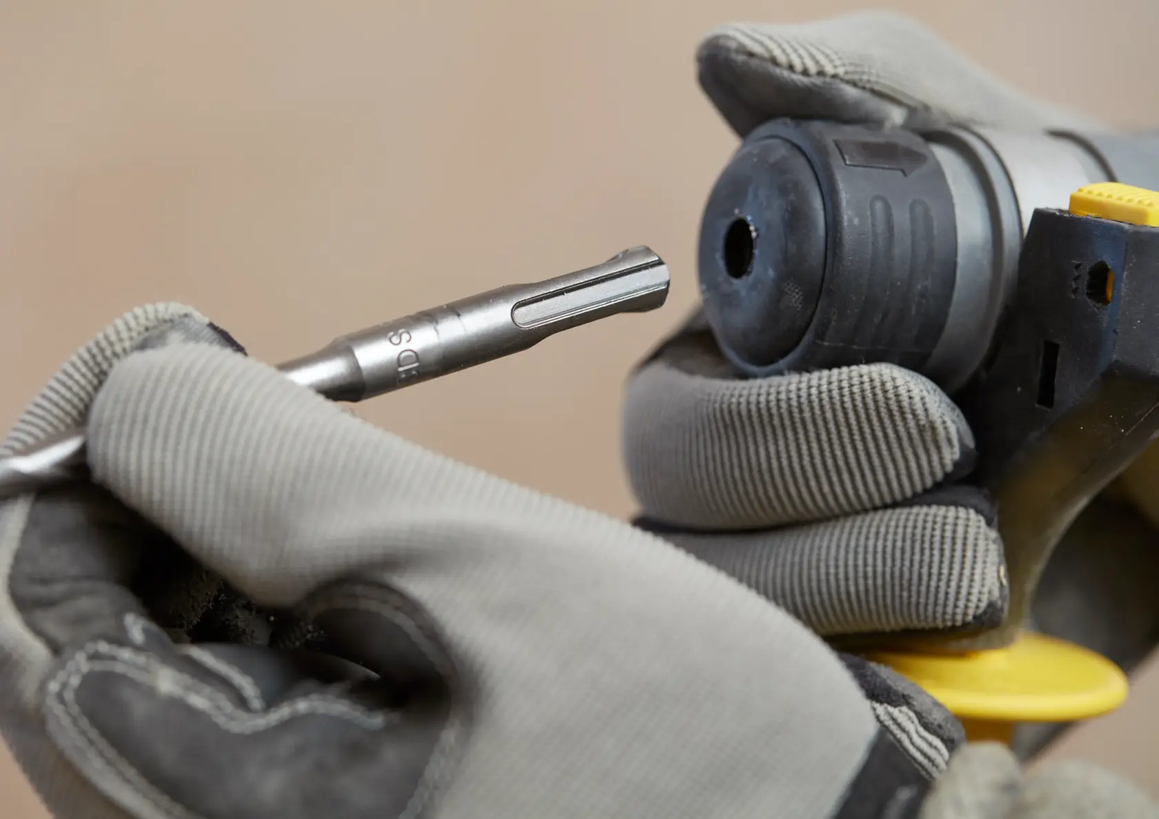Photo of STANLEY SFMCH900B rotary hammer with gloved hands inserting a drill bit, close-up angle.