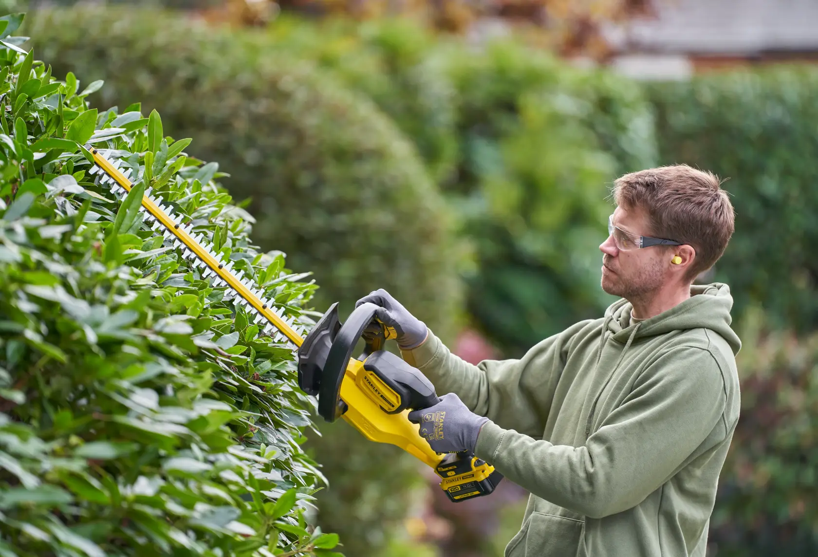 STANLEY SFMCHT655M1 hedge trimmer in use outdoors, trimming green hedges.