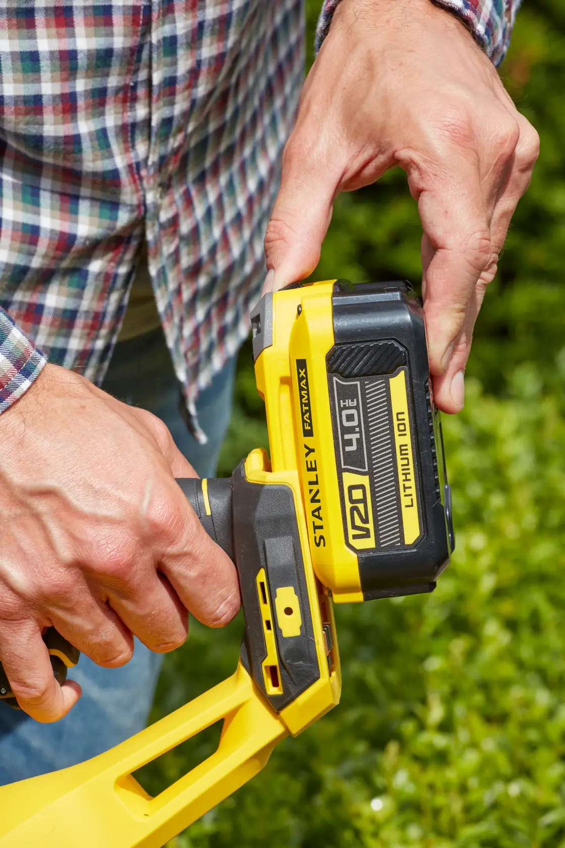 Photo of STANLEY SFMCHT855B V20 4.0Ah battery being attached to yellow cordless tool outdoors.