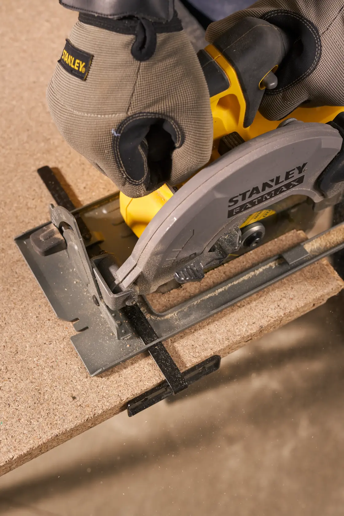 Photo of STANLEY SFMCK470D2 circular saw cutting wood, close-up view, user wearing work gloves.