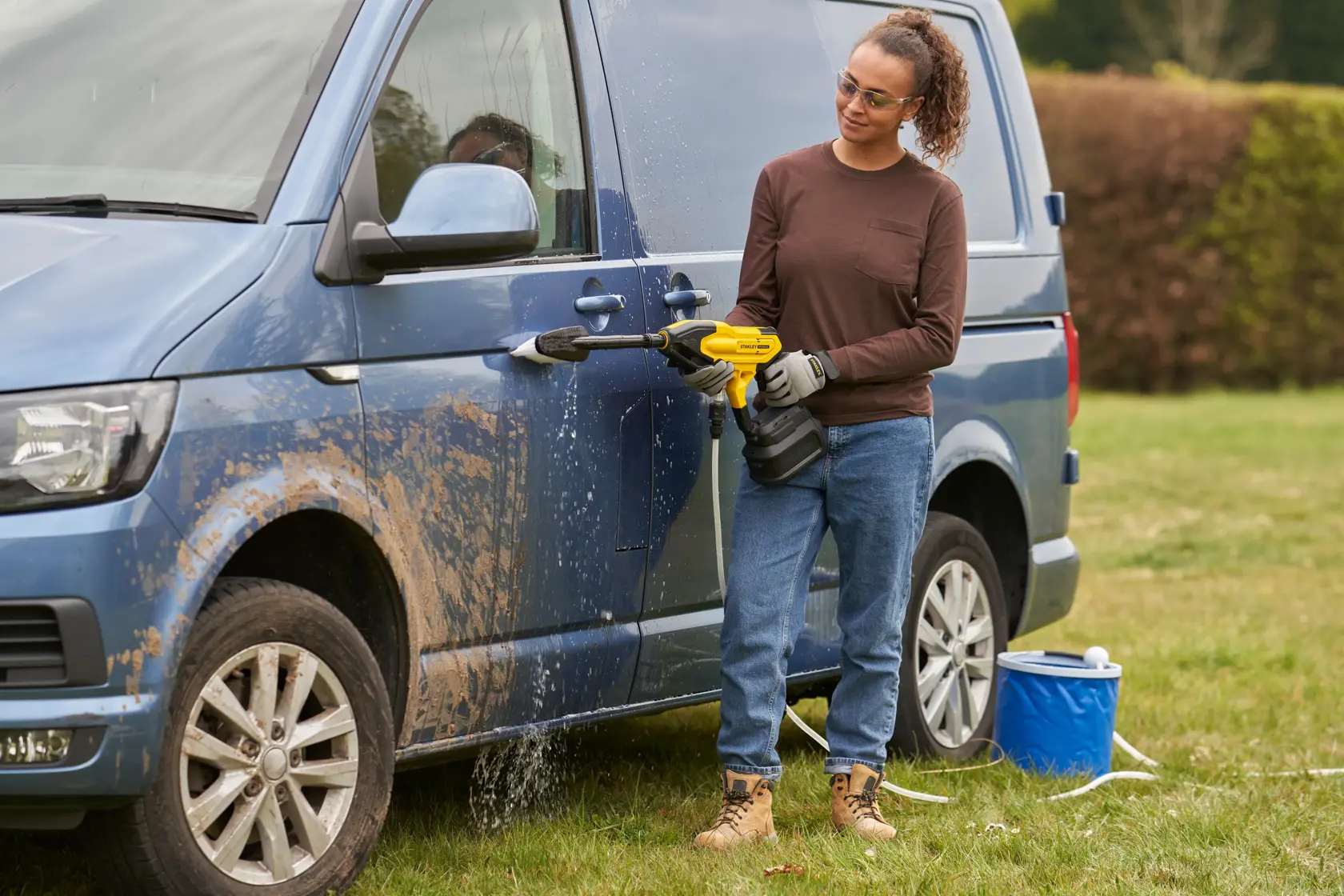 STANLEY SFMCPC93B portable washer used to clean muddy blue van outdoors, person holding tool.