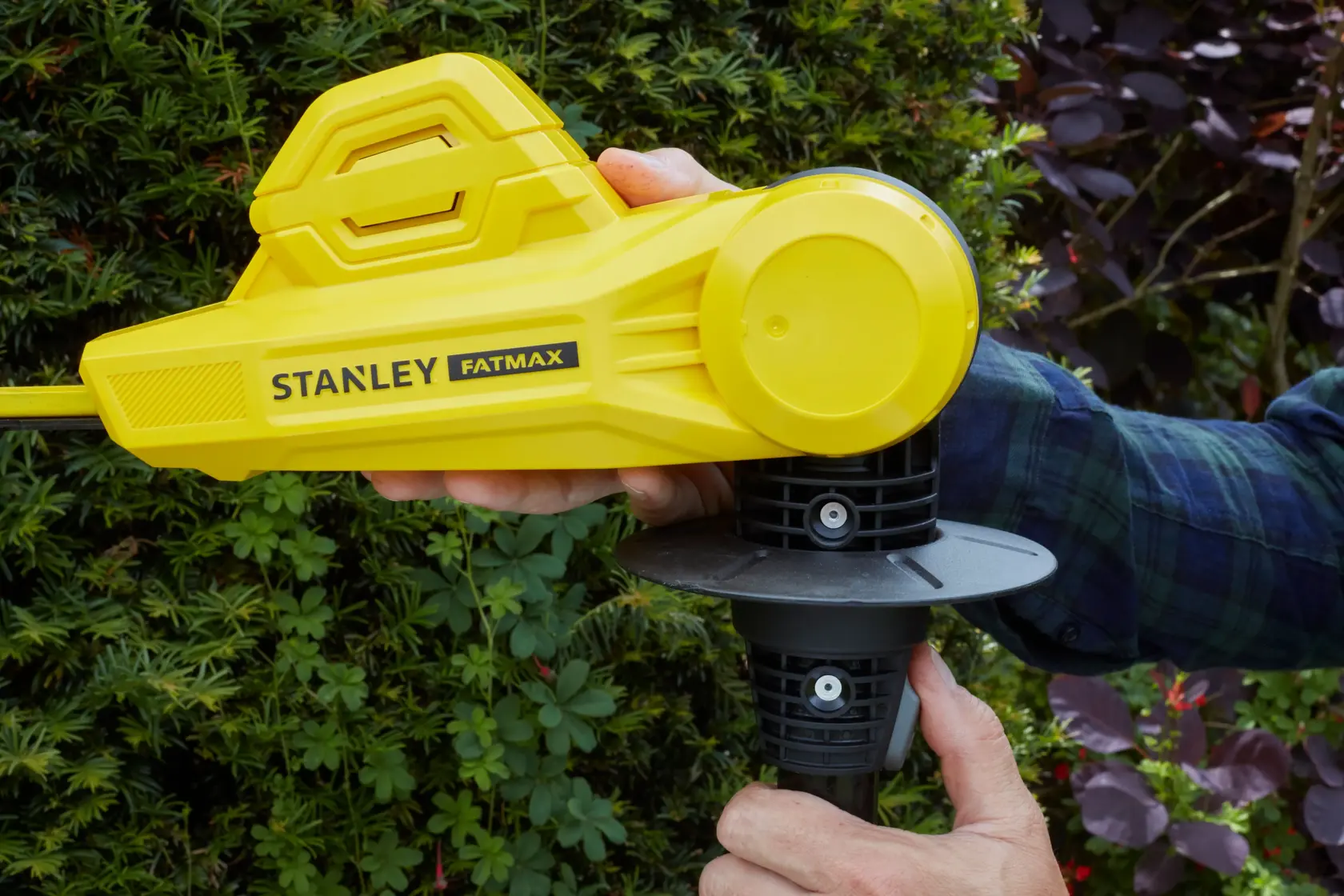 STANLEY SFMCPH845B yellow hedge trimmer side view in use, close-up with hand on handle outdoors.