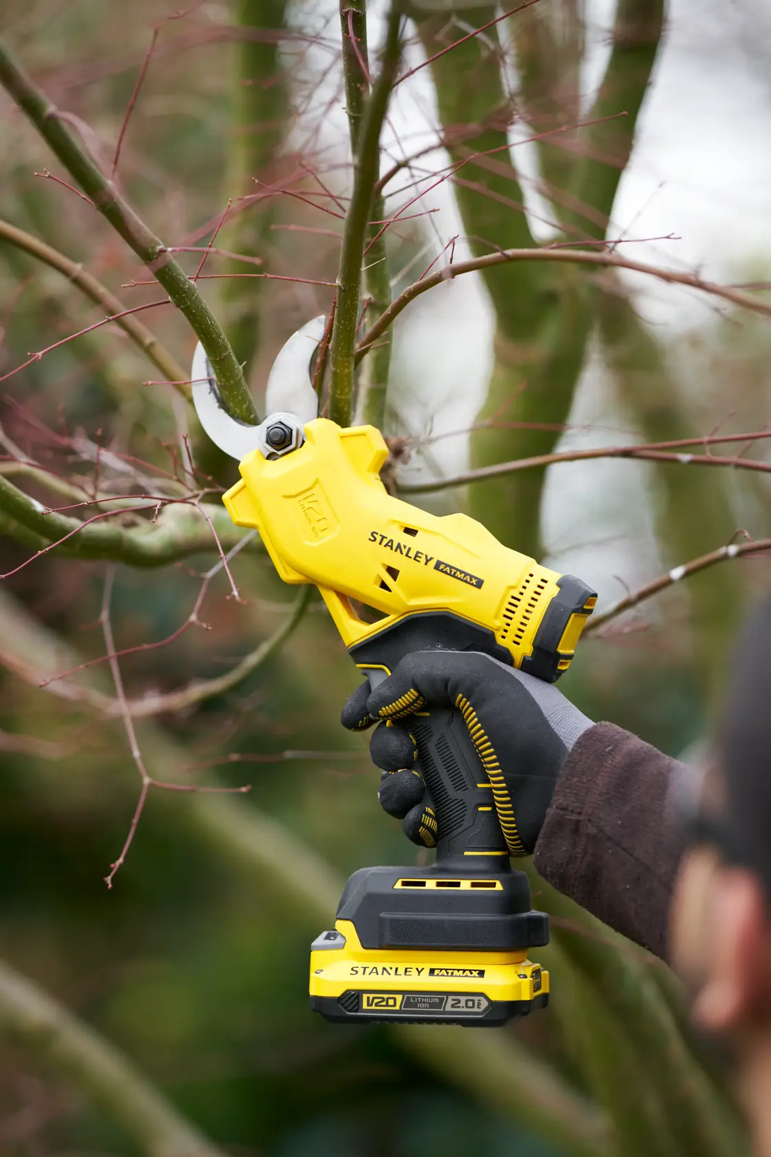 Photo of STANLEY SFMCPP32D1 cordless pruner cutting a tree branch, shown in use with gloved hand outdoors.