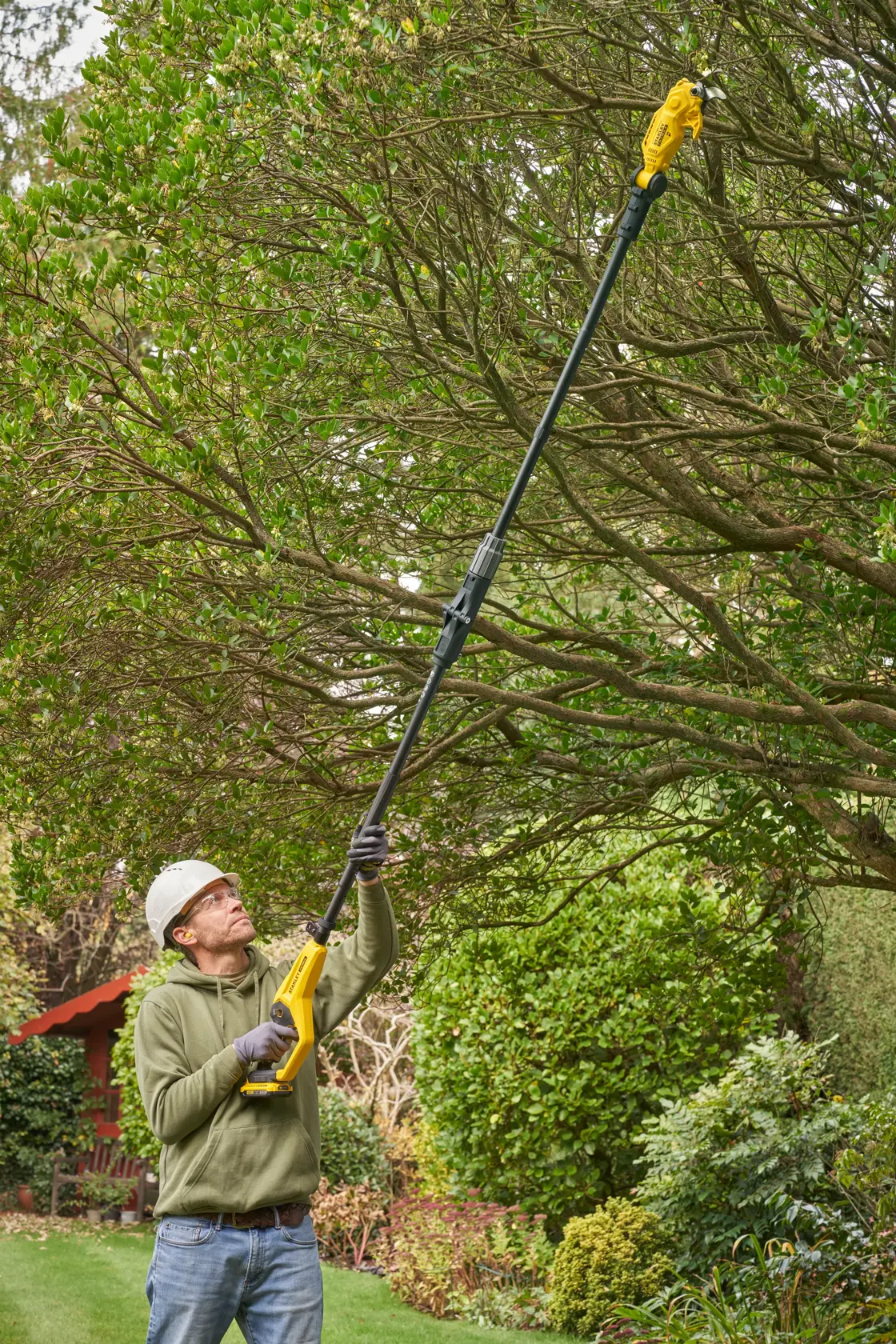 STANLEY SFMCPP632B cordless pole saw in use for tree pruning in a garden setting.