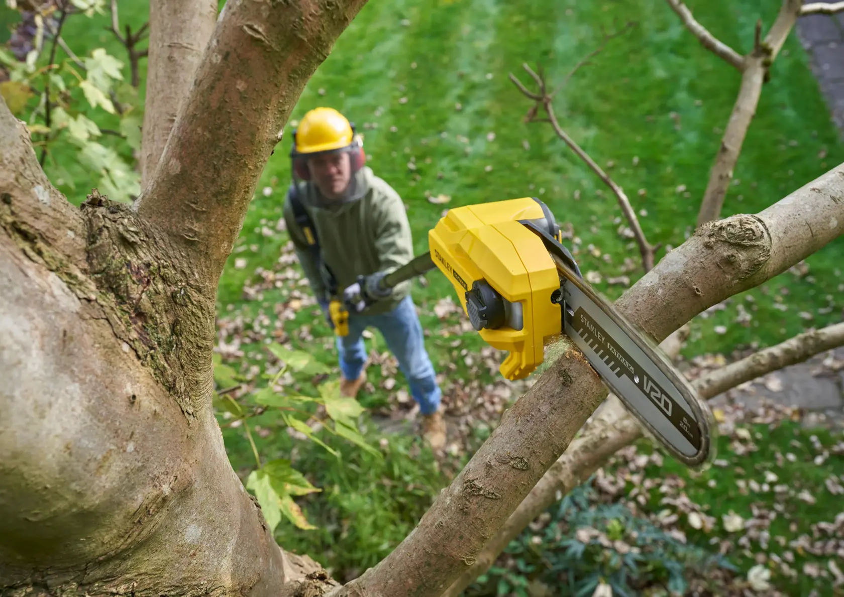 Photo of STANLEY SFMCPS720B-XJ pole saw in use cutting a tree branch, outdoor garden setting.