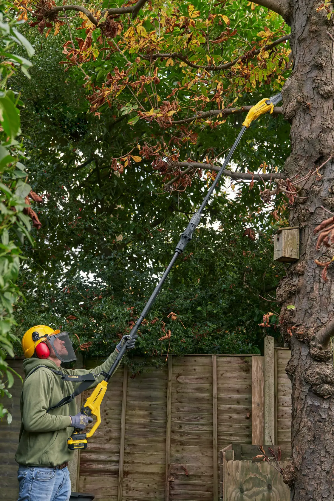 STANLEY SFMCPS720B-XJ pole saw used for pruning high tree branches in a garden setting.