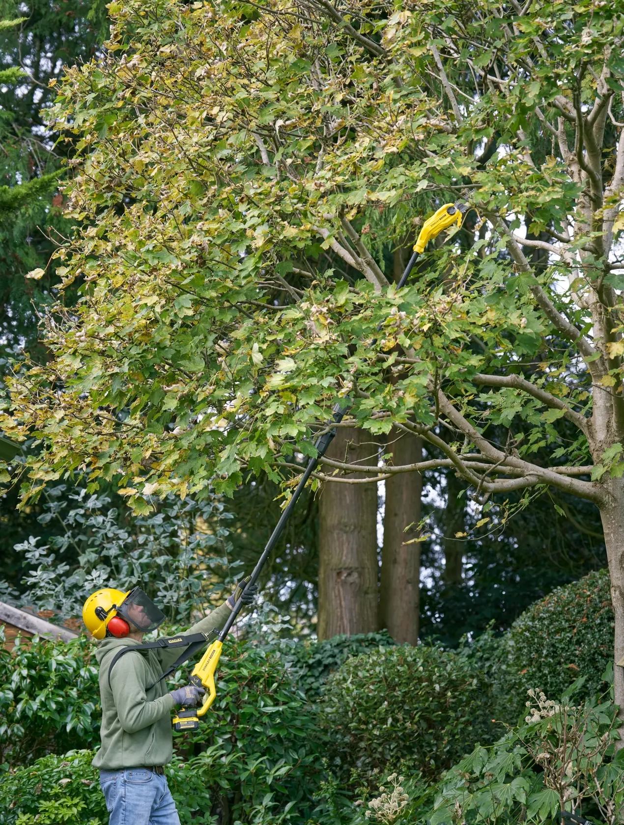 STANLEY SFMCPS720M1 pole saw used outdoors to trim tall tree branches, person wearing safety gear.