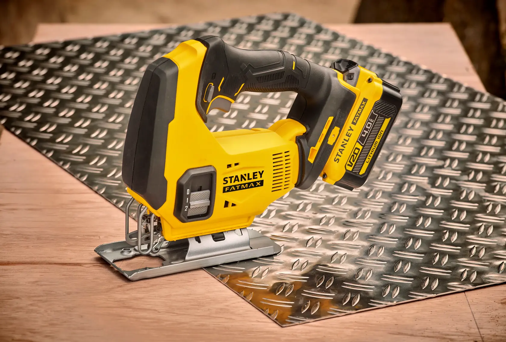 Photo of STANLEY SFMCS600B jigsaw on a metal sheet, yellow and black cordless power tool, side view.