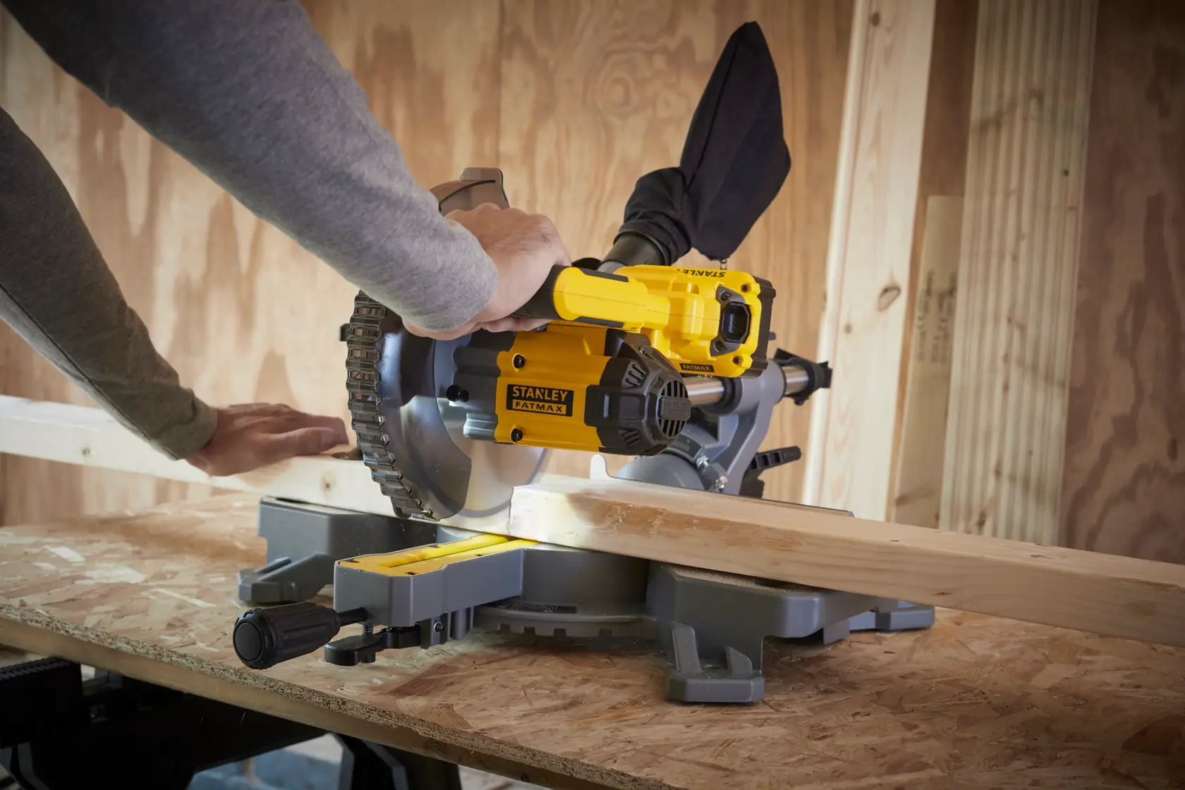 STANLEY SFMCS701B miter saw in use, cutting wood plank on a workbench in workshop.