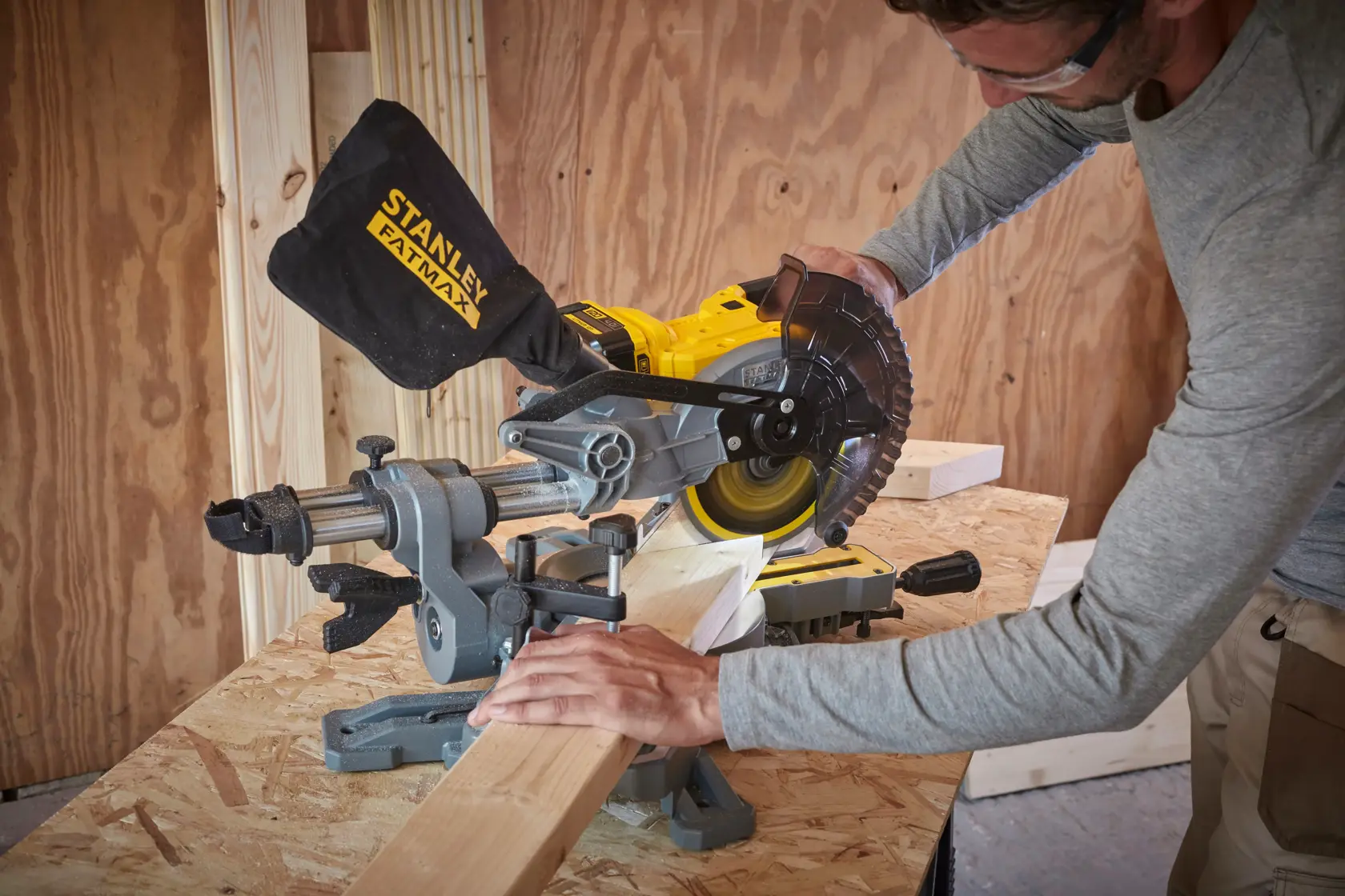 STANLEY SFMCS701M2 miter saw in use cutting wood on a workbench in workshop, angled side view.