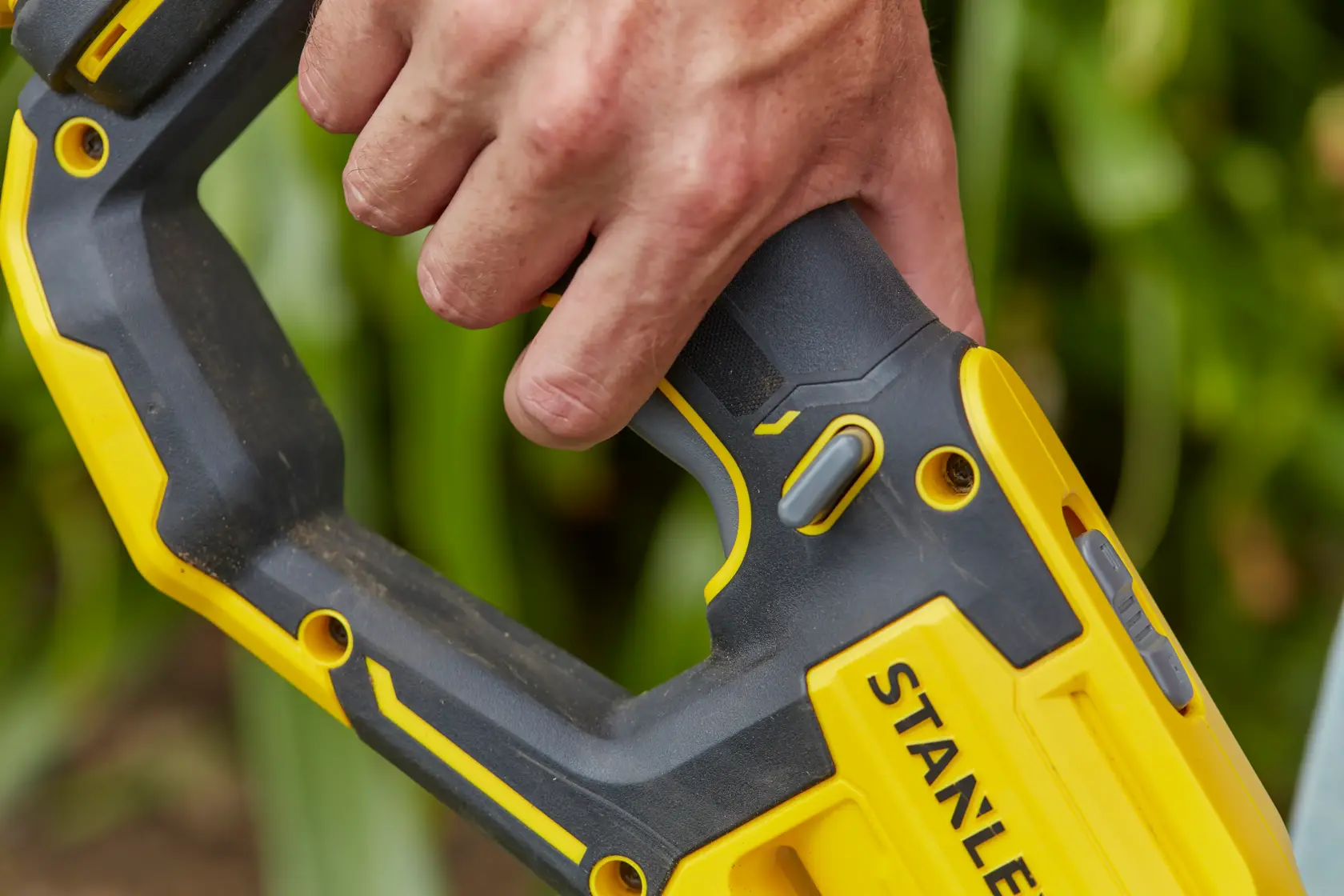 Close-up photo of a hand gripping the handle of a STANLEY SFMCST933M1 cordless power tool with yellow and black design.