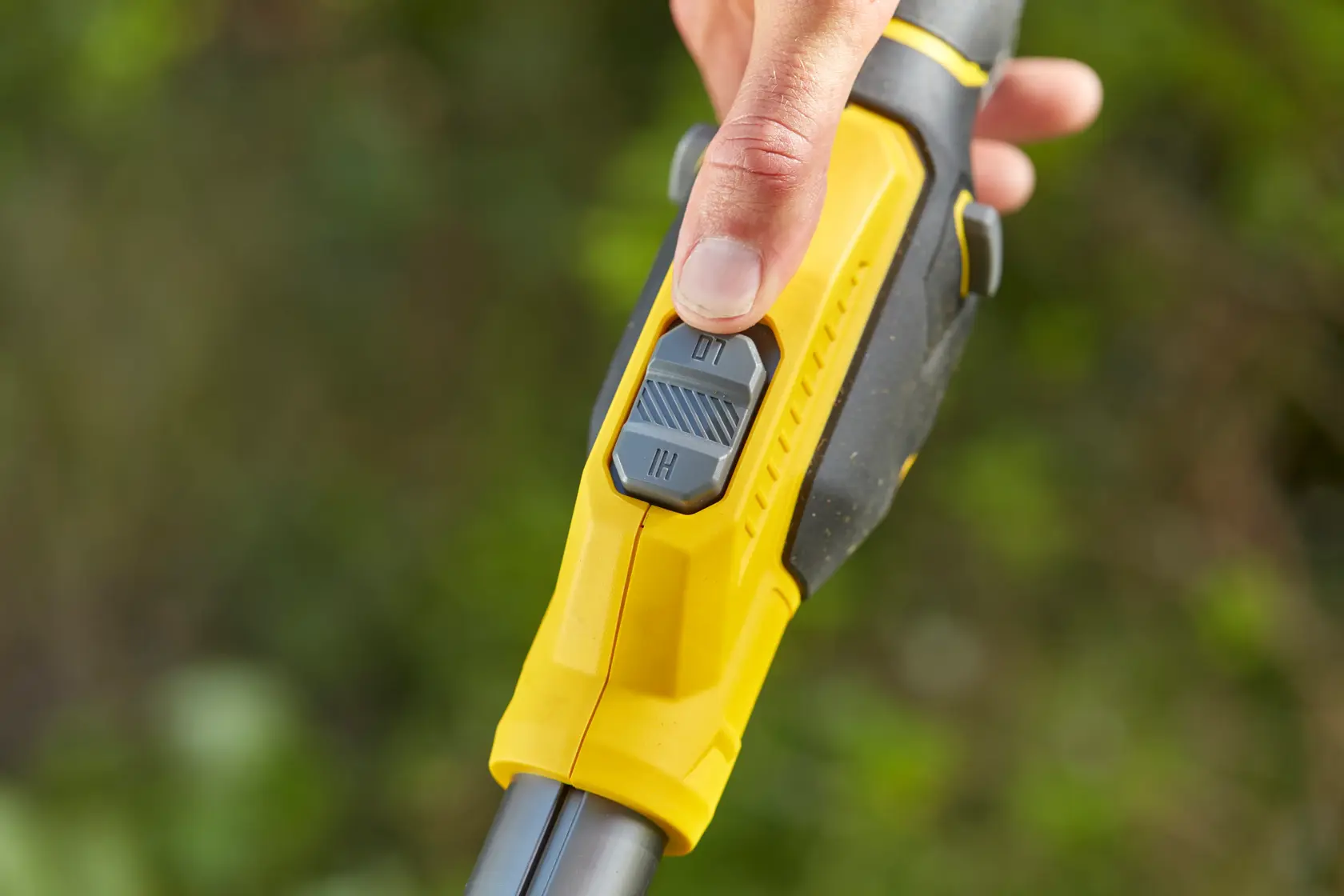 STANLEY SFMCSTB933B trimmer close-up of yellow and black handle with speed switch and thumb operation outdoors.