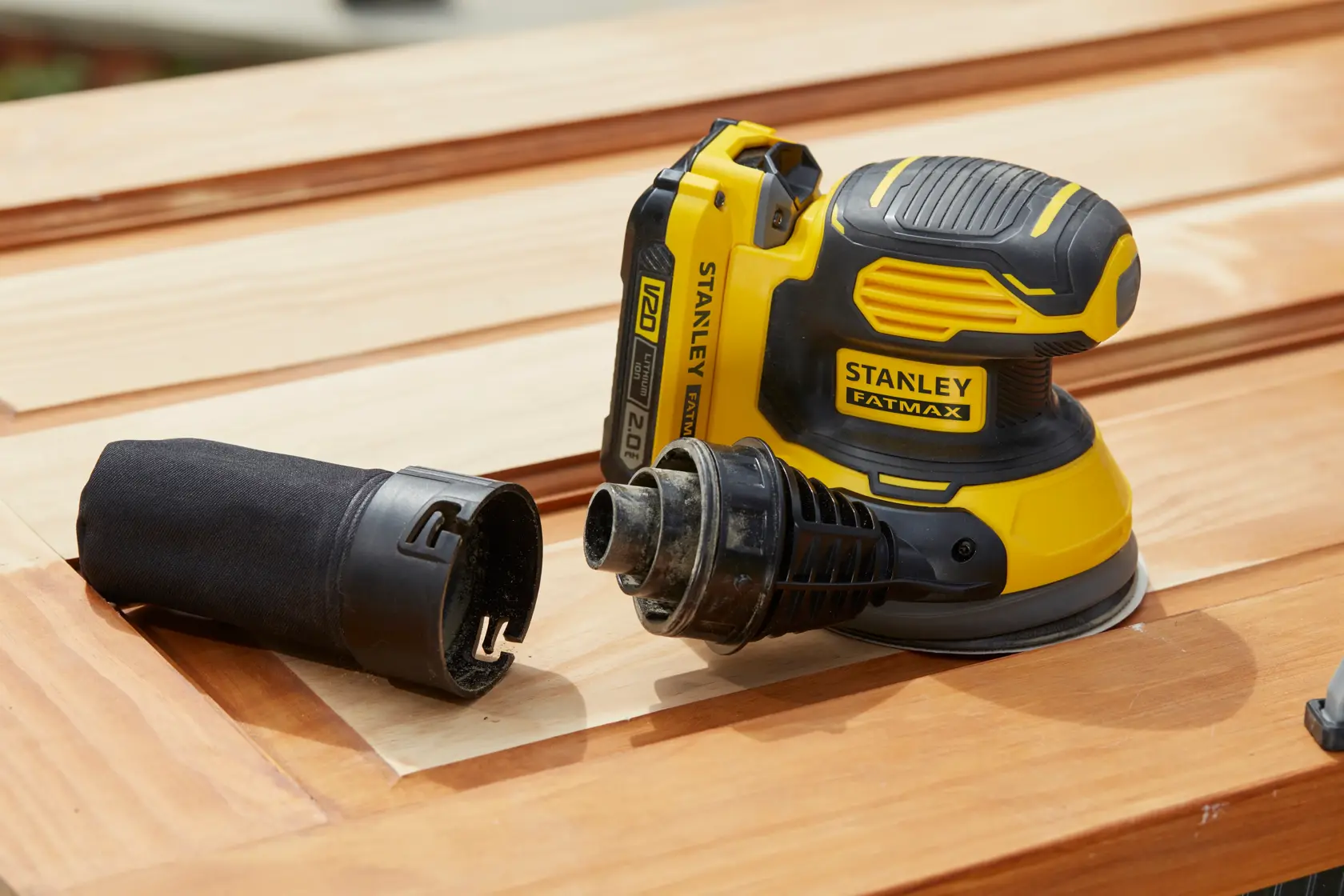 Stanley SFMCW220B cordless sander with dust port, yellow-black, on wooden surface, product photography.
