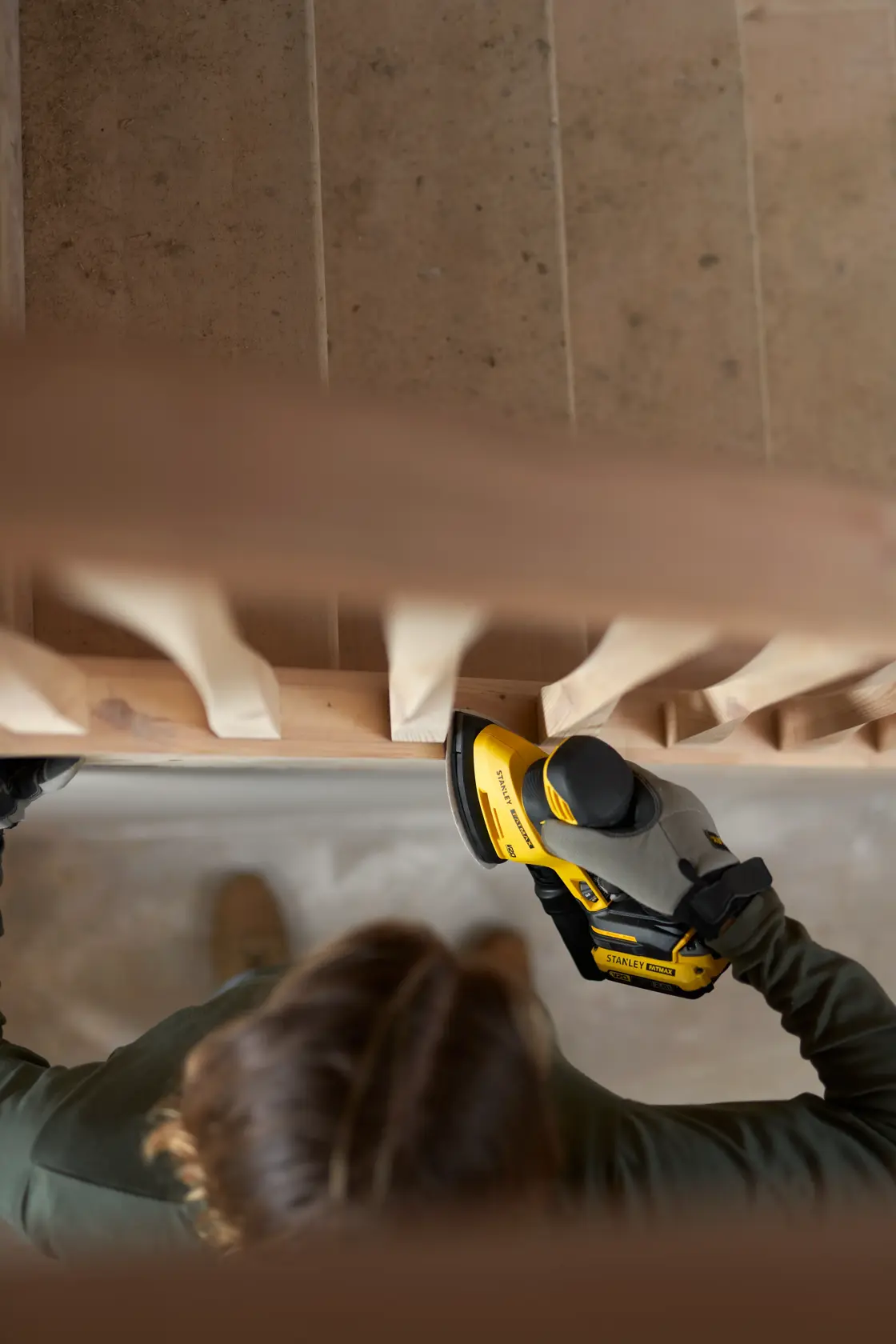 Photo of STANLEY SFMCW221B sander in use on a wooden staircase, hand holding tool for sanding railing.