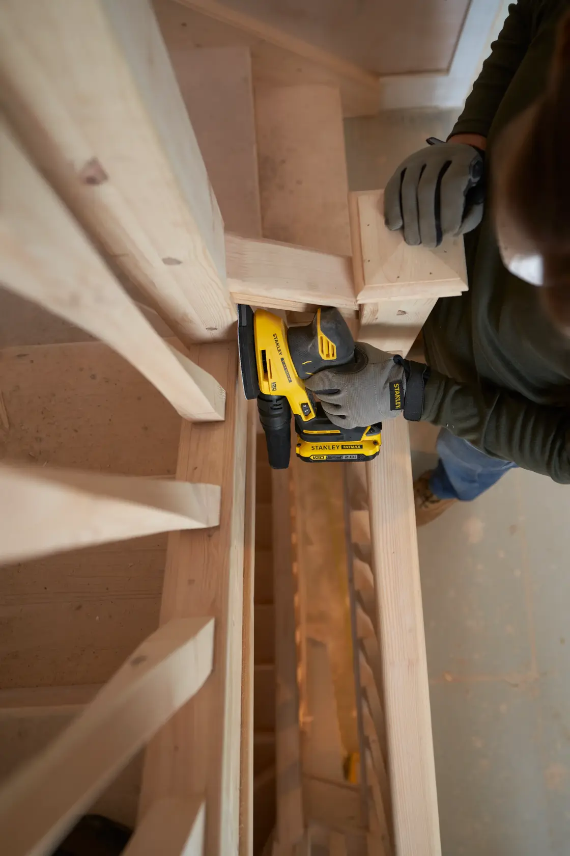 STANLEY SFMCW221B sander used on wooden stairs, close-up angle, operator wearing gloves.