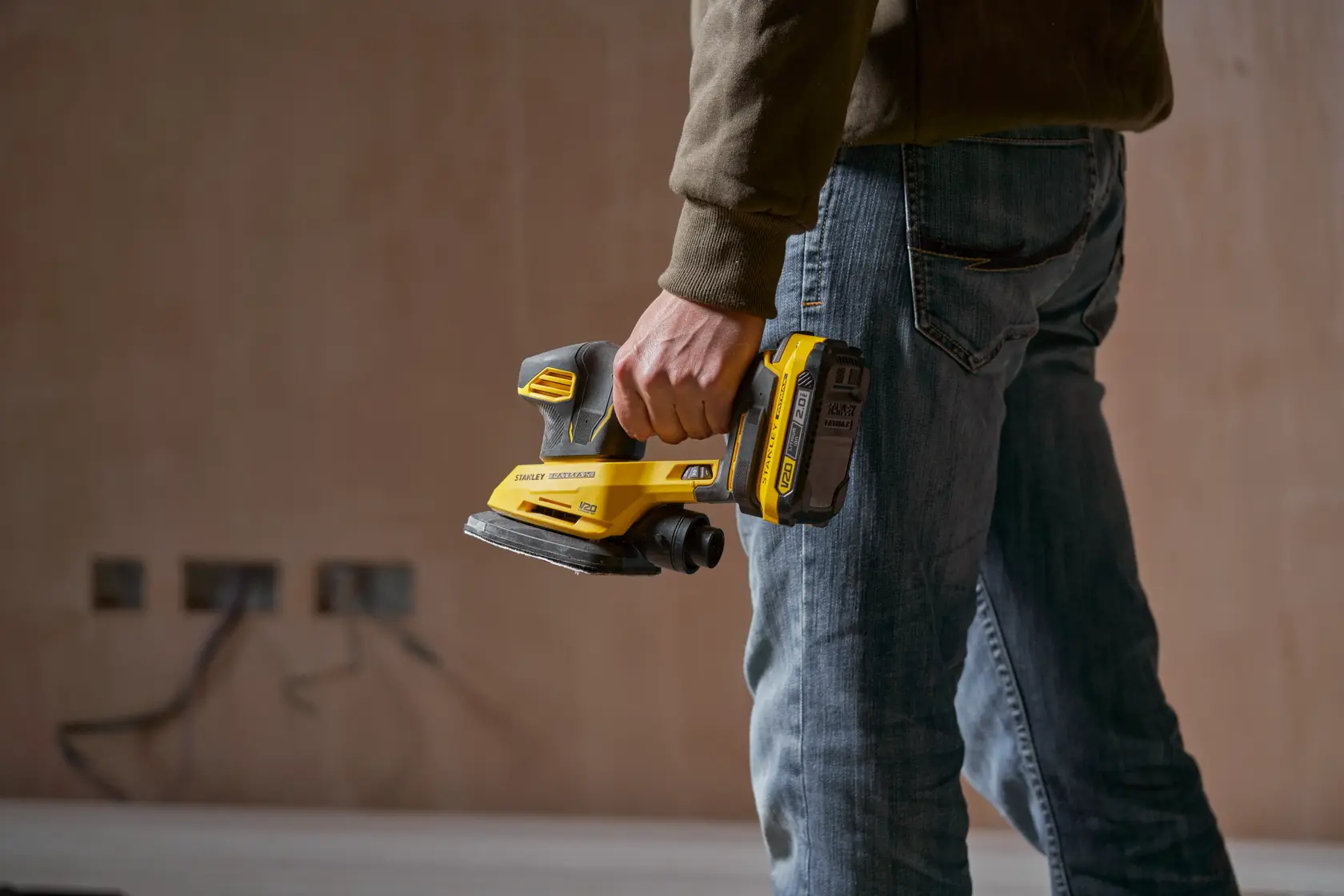 Photo of STANLEY SFMCW221B cordless sander held by a person in a workwear setting.
