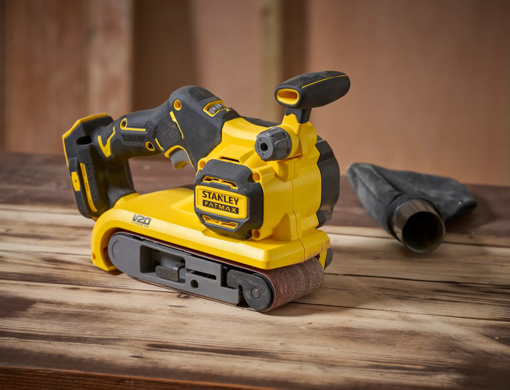 STANLEY SFMCW223B-XJ belt sander, yellow and black, side angle, on wooden surface.