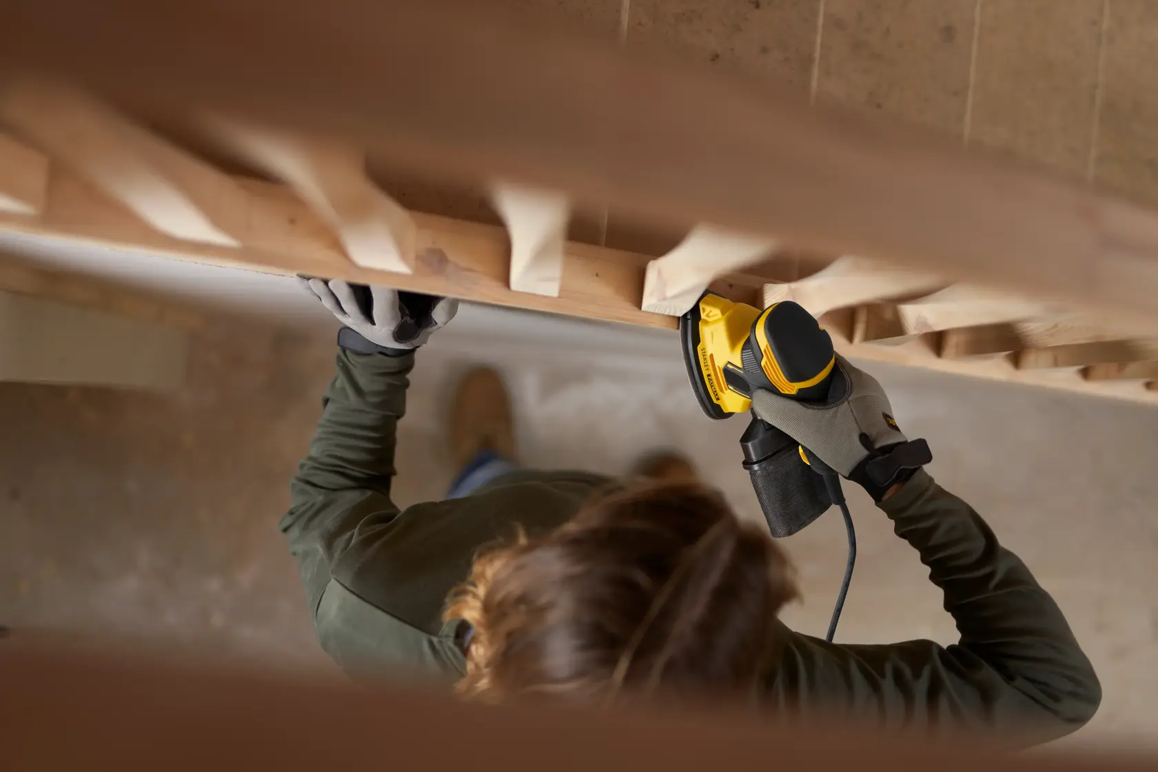 Person using STANLEY SFMEW210S sander on wooden staircase railing, top-down view.