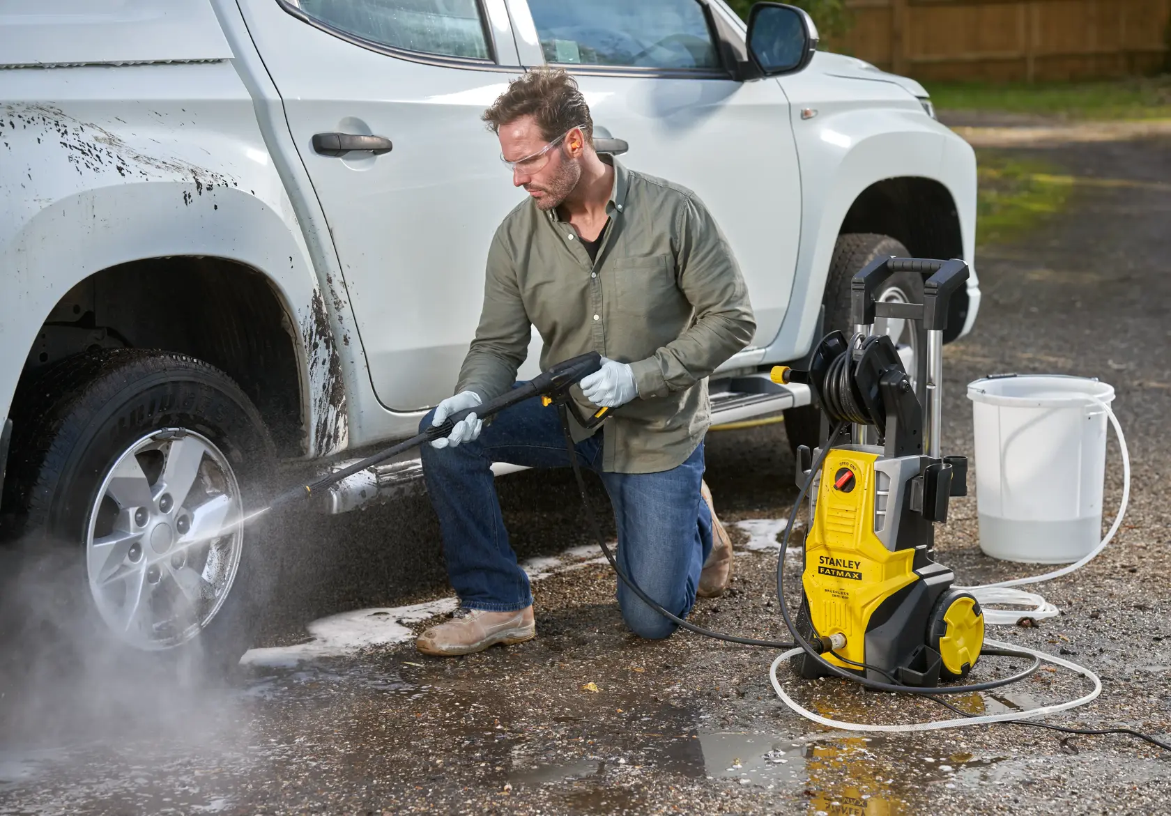 Stanley SFMPW2400 pressure washer cleaning car wheel outdoors; yellow unit, hose, bucket in scene.