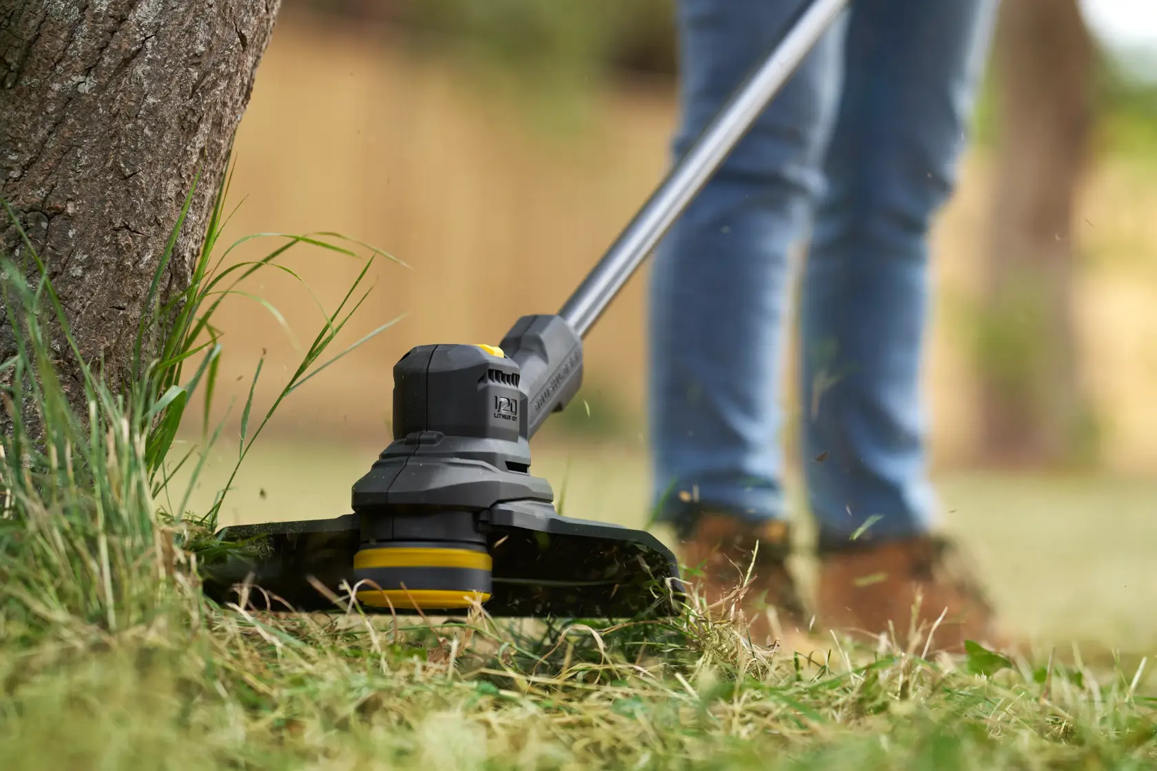STANLEY SFMSTB930M grass trimmer close-up in use, cutting grass around a tree in a garden.