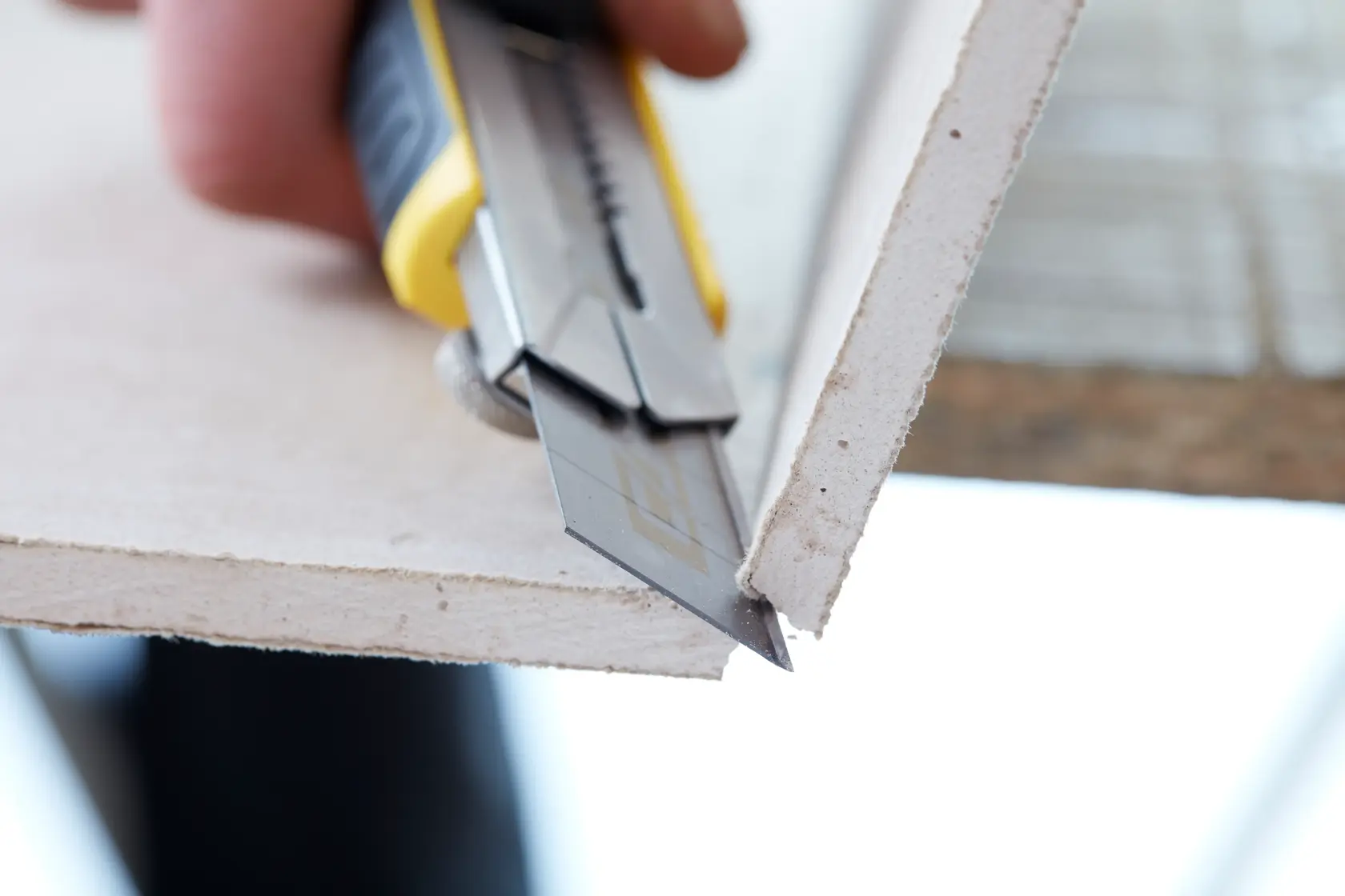Stanley STHT0-11825 utility knife cutting drywall, close-up photo, yellow and black handle.