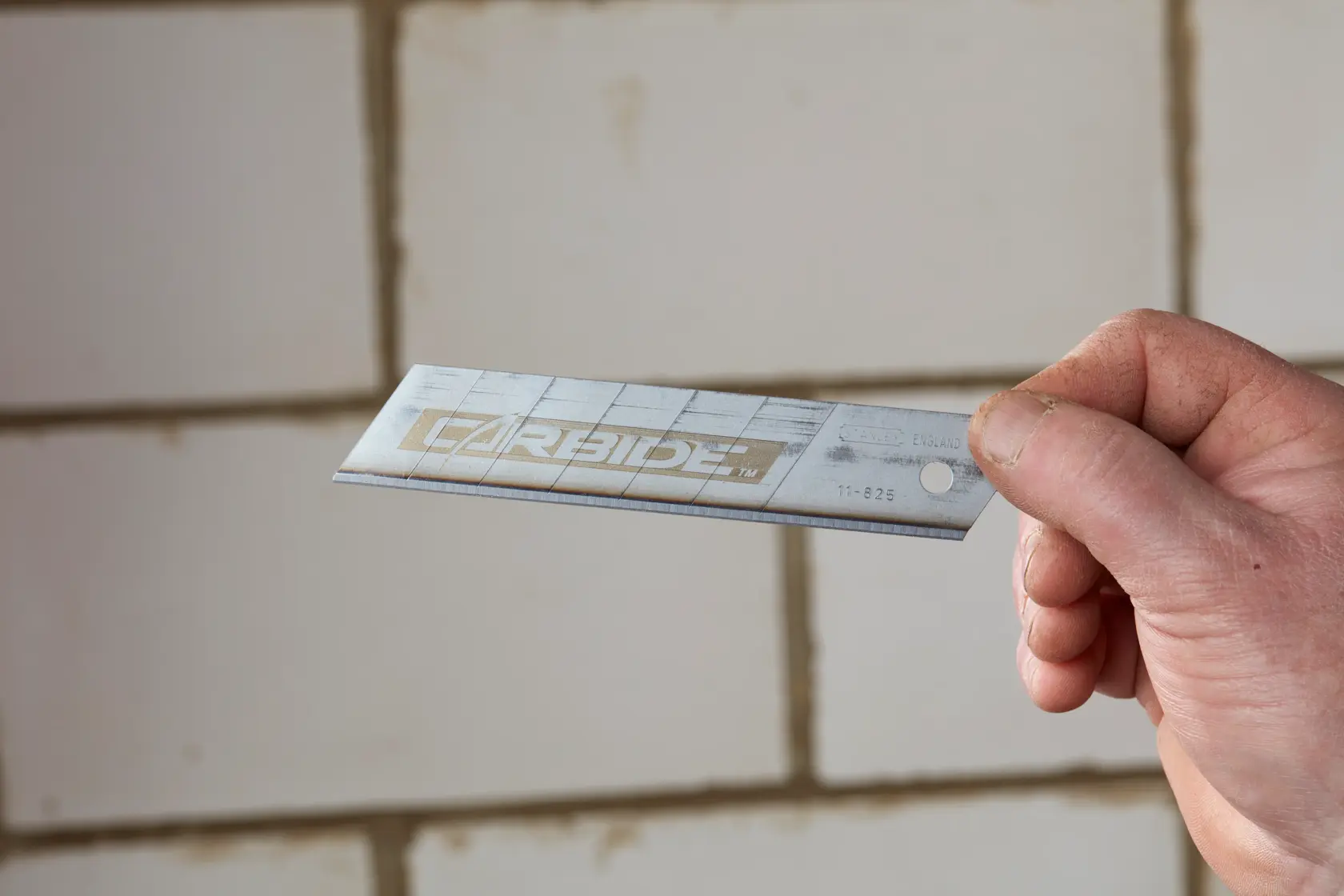 STANLEY STHT0-11825 utility blade held in hand, silver color, with CARBIDE marking visible.