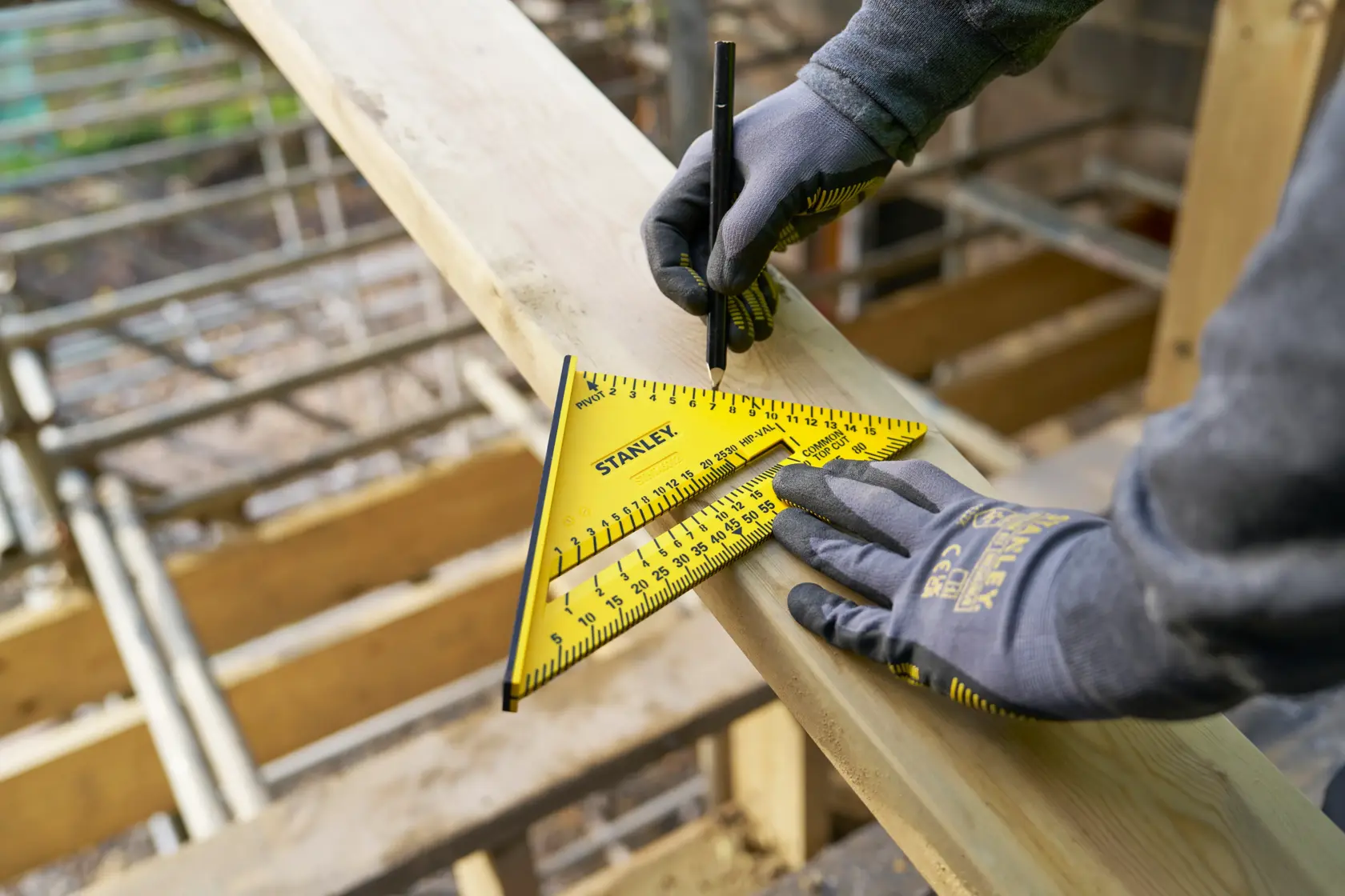 Photo of STANLEY STHT46012-0 yellow rafter square on wood plank, worker marking with pencil, construction site.