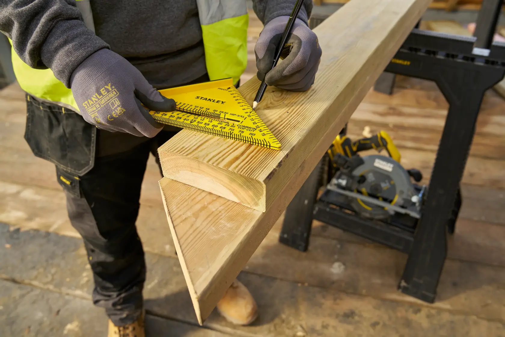 STANLEY STHT46012-0 yellow layout square used to mark wood beam on construction site, close-up angle.
