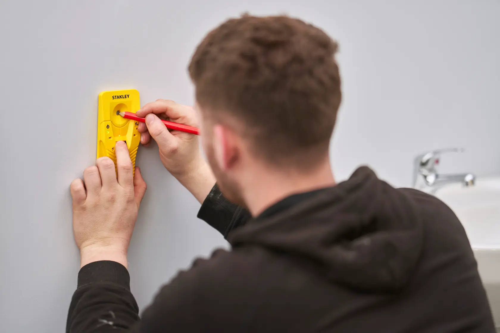 STANLEY STHT77587-0 digital stud finder in use on wall near sink, yellow handheld device, photography.
